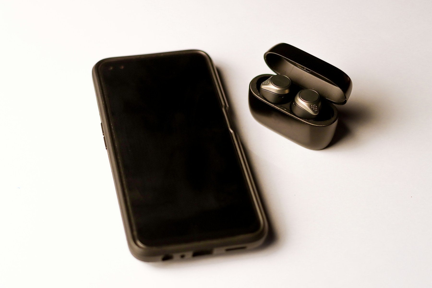 Black smartphone beside wireless earbuds on a light surface